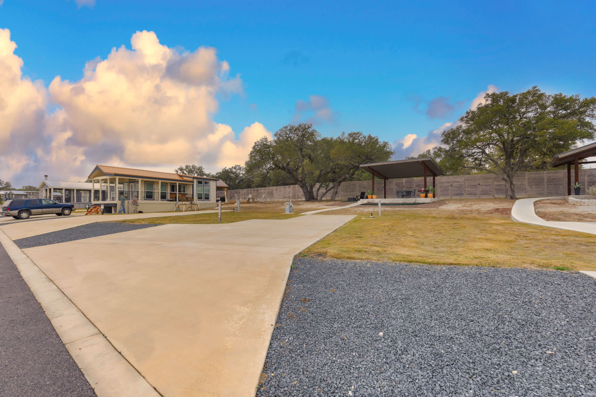 Executive RV Site 062 at Firefly Hill Country — concrete pad, covered pavilion and live oaks under a Hill Country sky